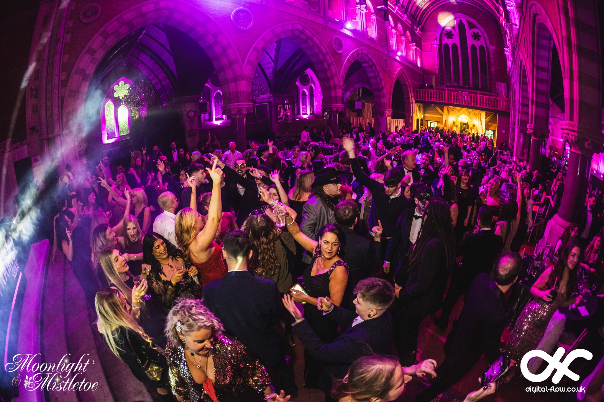 Guests dancing at a Moonlight & Mistletoe Christmas party night at Empire Banqueting Hall Leicester, with the venue's Gothic arches lit in purple